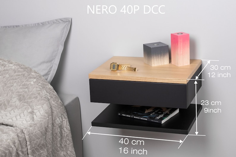 May include: A black floating bedside table with a drawer and a lower shelf. The nightstand is 40 cm wide, 23 cm deep, and 30 cm tall. It has a wood top and is shown with a watch, two decorative boxes, and a book on the shelf.