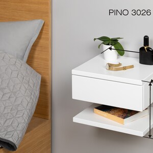 May include: White floating nightstand with a drawer and a shelf. The nightstand is 12 inches wide, 10 inches deep, and 9 inches tall. It is labeled "PINO 3026 P-B".