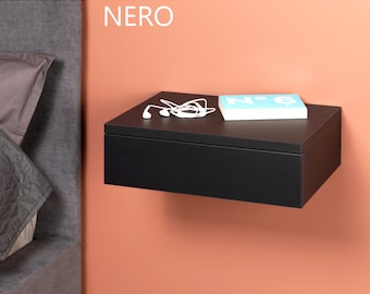 May include: A black floating bedside table with a drawer, a book, and white headphones on top. The bedside table is mounted on a peach wall.
