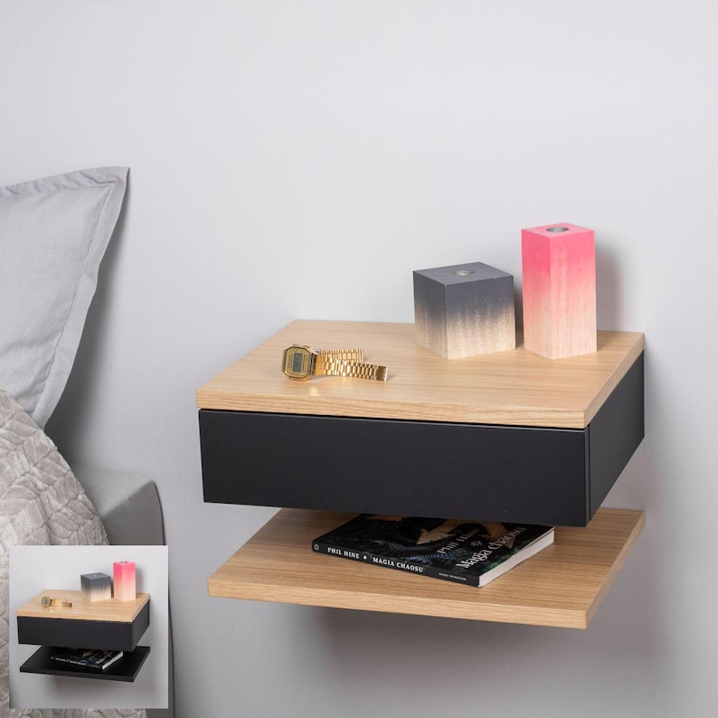 May include: A floating bedside table with a black drawer and a wooden top. The bedside table has a lower shelf and is decorated with a watch, a book, and two decorative blocks. One block is grey with a gradient and the other is pink with a gradient.