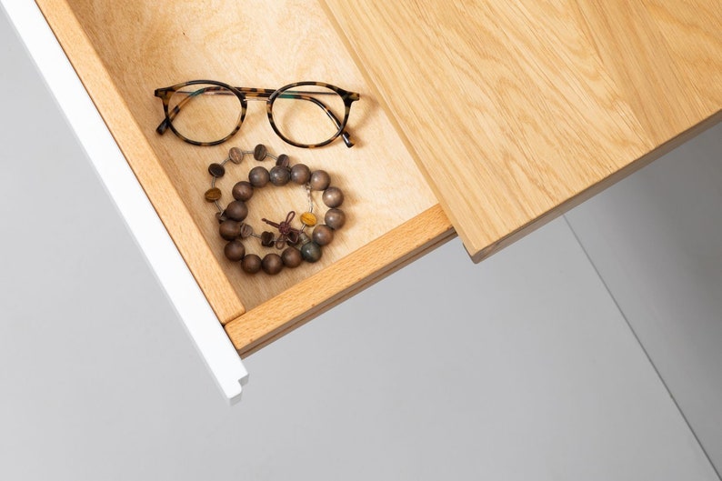 May include: A wooden drawer with a light wood finish is open, revealing a pair of tortoiseshell eyeglasses and a brown wooden beaded bracelet.