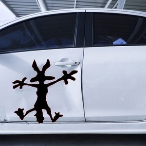 May include: A white car with a black silhouette of a cartoon character on the side door. The character has long arms and legs and is in a running pose.