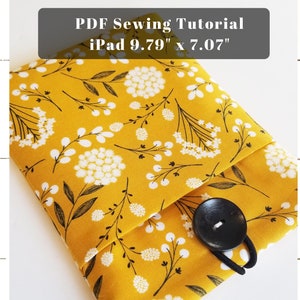 Könnte beinhalten: Eine gelbe iPad-Hülle aus Stoff mit einem weißen Blumenmuster und einem schwarzen Knopfverschluss. Die Hülle ist für ein iPad mit den Maßen 9,79 Zoll x 7,07 Zoll konzipiert. PDF-Näh-Anleitung.