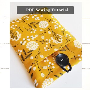 Peut inclure: Une pochette en tissu jaune avec un motif floral blanc et une fermeture à bouton noir. La pochette est pliée en deux et le bouton est visible. Le texte "PDF Sewing Tutorial" est en haut de l'image.