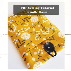 May include: A yellow fabric case with a floral pattern and a black button closure. The case is designed for a Kindle Oasis e-reader. The text "PDF Sewing Tutorial Kindle Oasis" is displayed above the case.