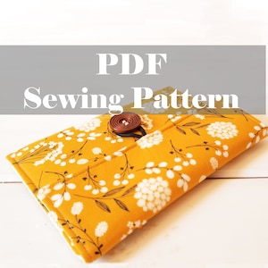 May include: PDF Sewing Pattern for a mustard yellow fabric wallet with a white floral print and a brown button closure.