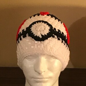 May include: White crochet beanie with a black and red Pokeball design.