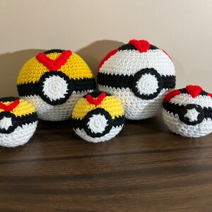 May include: Four crocheted Poke Balls in different sizes. The largest is white with black and red accents. The other three are yellow, black, and red.
