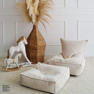 May include: A neutral nursery setting with a white rocking horse, a woven basket vase with dried plants, and a corduroy beanbag chair and ottoman. The wall reads "WHAT MAKES KIDS HAPPY".