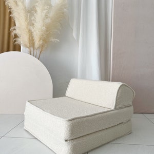 May include: A white, fluffy, foldable chair with a rounded back. The chair is made of a soft, plush fabric and is perfect for lounging or sleeping.