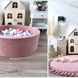 May include: A pink velvet ball pit with a ruffled edge, filled with pastel colored balls. The pit is in a room with a wooden dollhouse and other decor.