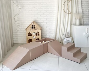 May include: A beige play set for children, featuring a ball pit, a slide, and steps. The set is made of soft foam and is perfect for indoor play.