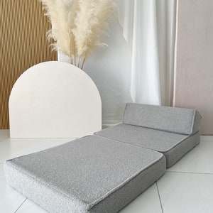 May include: A gray, foldable floor cushion with a tufted backrest. The cushion is made of a soft, fuzzy fabric and is perfect for lounging or sitting on the floor.