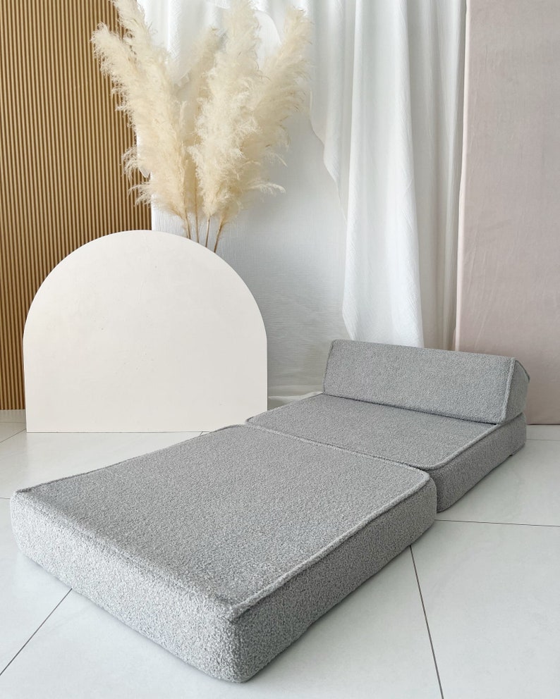 May include: A gray, foldable floor cushion with a tufted backrest. The cushion is made of a soft, fuzzy fabric and is perfect for lounging or sitting on the floor.