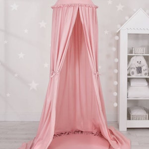 Puede incluir: Una tienda de campa&ntilde;a de tela rosa con un borde con volantes y una alfombra redonda rosa a juego. La tienda est&aacute; montada en una habitaci&oacute;n con una pared blanca y estrellas blancas.