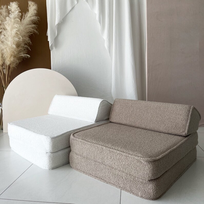 May include: Two foldable futon style beds, one white and one brown, are shown against a white backdrop. The beds are made of a soft, plush fabric and have a simple, modern design.