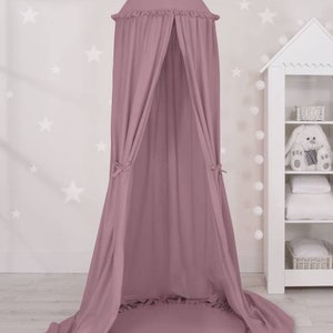 Puede incluir: Una tienda de campa&ntilde;a de color rosa polvoriento con un borde con volantes. La tienda est&aacute; hecha de un tejido suave y ligero, ideal para crear un espacio acogedor y privado para un ni&ntilde;o.
