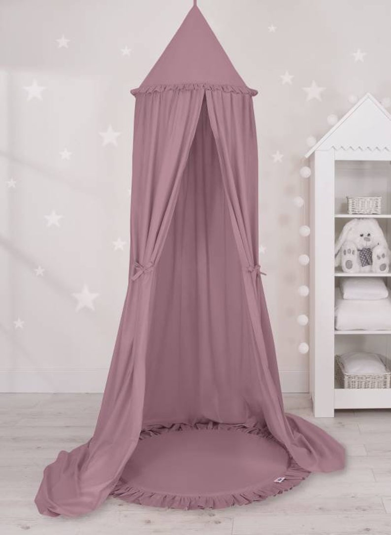 Puede incluir: Una tienda de campa&ntilde;a de color rosa polvoriento con un borde con volantes. La tienda est&aacute; hecha de un tejido suave y ligero, ideal para crear un espacio acogedor y privado para un ni&ntilde;o.
