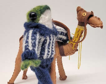 De handgebreide kikker, gekleed in een gestreepte trui en baggy jeans, zou dolgraag een nieuw thuis vinden!