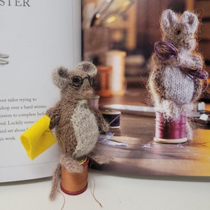 May include: Two brown knitted mice wearing glasses, one holding a yellow piece of fabric, sitting on spools of thread.