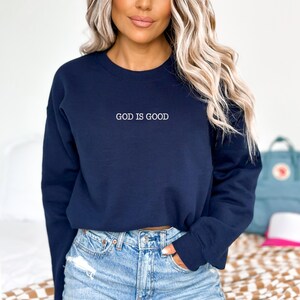 May include: A navy blue cropped sweatshirt with the text "GOD IS GOOD" in white lettering.