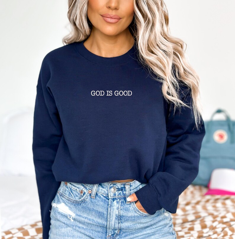 May include: A navy blue cropped sweatshirt with the text "GOD IS GOOD" in white lettering.