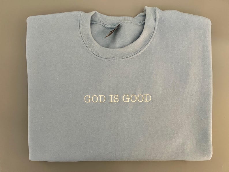 May include: A light blue sweatshirt with the text "GOD IS GOOD" embroidered in white on the front.