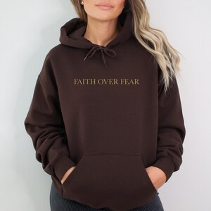 May include: A brown hooded sweatshirt with the text "FAITH OVER FEAR" printed in gold on the front.