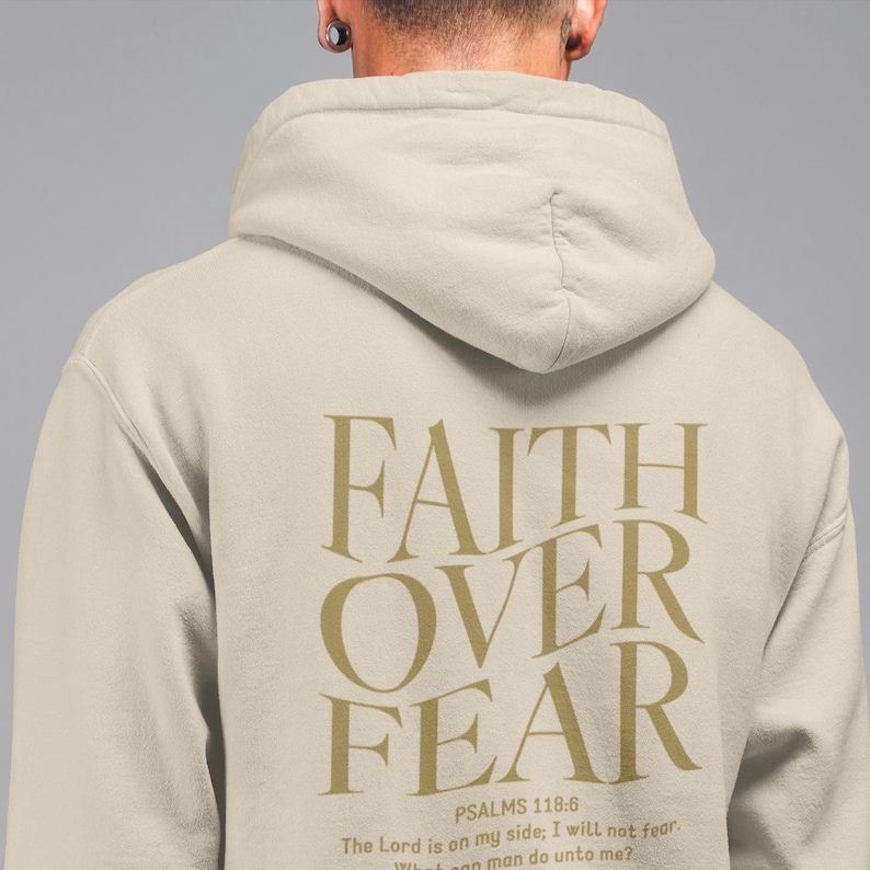 May include: A beige hoodie with the words "FAITH OVER FEAR" printed in gold on the back. The text is accompanied by the Bible verse "PSALMS 118:6 The Lord is on my side; I will not fear. What can man do unto me?"