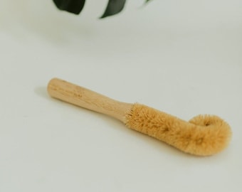 May include: A wooden handled brush with a curved, natural bristle head. The brush is designed for cleaning bottles.