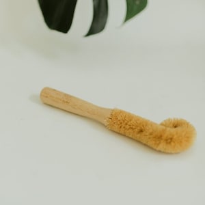May include: A wooden handled brush with a curved, natural bristle head. The brush is designed for cleaning bottles.