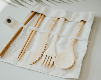 May include: A set of bamboo utensils, including a fork, knife, spoon, chopsticks, and a straw, are neatly organized in a white canvas carrying case.