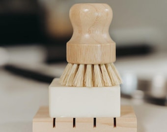 May include: A wooden dish brush with a natural bristle brush head and a wooden soap dish with a bar of soap. The dish brush and soap dish are on a wooden countertop.
