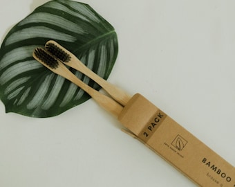 May include: Two brown bamboo toothbrushes with black bristles in a cardboard box labeled "2 PACK" and "BAMBOO TOOTHBRUSHES" with a green leaf icon.