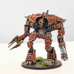 May include: A detailed miniature robot figure, primarily red and gold, with intricate mechanical details. The figure has a skull-like face and claw-like hands. It stands on a circular base with small patches of green vegetation. The robot is a collectible item.