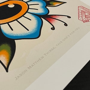 May include: A blue and green floral tattoo design with a large eye in the center. The design is surrounded by a banner with the text "Never Enough". The image also includes a red stamp with the text "TOM STITCH 2023" and the text "JASON MATTHEW THIRSK, THIS ONE'S FOR YOU".