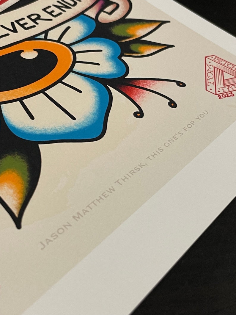 May include: A blue and green floral tattoo design with a large eye in the center. The design is surrounded by a banner with the text "Never Enough". The image also includes a red stamp with the text "TOM STITCH 2023" and the text "JASON MATTHEW THIRSK, THIS ONE'S FOR YOU".