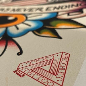 May include: Red triangle logo with the text "Tom Beichley Tattoo" and the year "2023" printed on a white background.