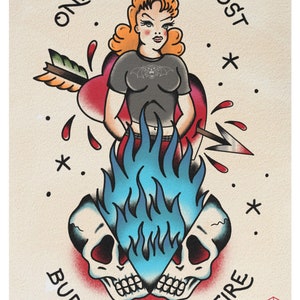 May include: A vintage-style tattoo illustration of a woman with red hair standing in blue flames. The woman is wearing a black t-shirt with a bat and a skull design. The text "ONLY A LOVER LOST BURNS IN GHOSTFIRE" is written around the image.