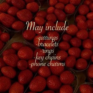 May include: A close-up of fresh, ripe strawberries in clear plastic containers. The image includes text that reads "May include - earrings - bracelets - rings - key chains - phone charms."