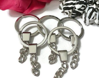 May include: Four silver keychains with a round ring and a chain attached. The chains have a small silver charm at the end.