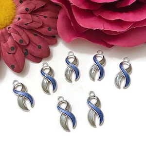 May include: Seven silver-toned awareness ribbon charms with blue enamel accents. The charms are arranged on a white surface, with a large pink flower in the background. The ribbon design is a symbol of support for various causes.
