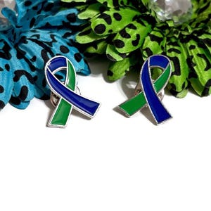 May include: Two enamel pins in the shape of a blue and green ribbon. The pins are on a white background.