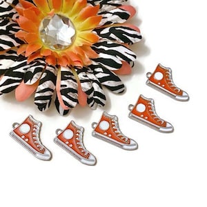 May include: Five orange and silver metal charms shaped like high-top sneakers. The charms have a white circle on the side of each shoe.
