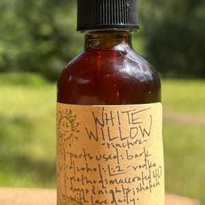 May include: A brown glass bottle with a black dropper top, labeled "White Willow" tincture. The label includes handwritten text detailing ingredients and preparation. The bottle is filled with a dark liquid.