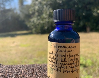 May include: A small blue glass bottle with a black lid and a brown paper label. The label says "WORMWOOD -tincture- parts) used: leaves alcohol: 1:3 [vodka] Method: macerated 4 days & nights: shaken with love daily.  Alchemista elrinth"