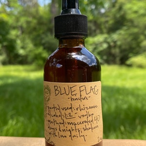May include: A brown glass bottle with a black dropper top and a paper label that reads "BLUE FLAG - tincture". The label also includes instructions for making the tincture, which include using rhizome, vodka, and macerating for 40 days and nights.