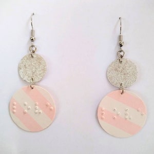 May include: A pair of silver and pink earrings with a striped pattern and braille dots. The earrings are made of two circular pieces, one silver and one pink with white stripes.