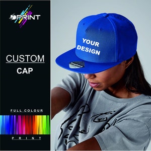 Könnte beinhalten: Eine blaue Baseballkappe mit einem weißen Druckknopfverschluss und dem Text "YOUR DESIGN" auf der Vorderseite.