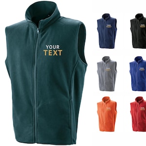 Pode incluir: Um colete de lã polar verde-azulado com zíper completo e gola alta. O texto "YOUR TEXT" é bordado no peito. Colete adicionais em azul marinho, preto, cinza, azul, laranja e vermelho também são exibidos.